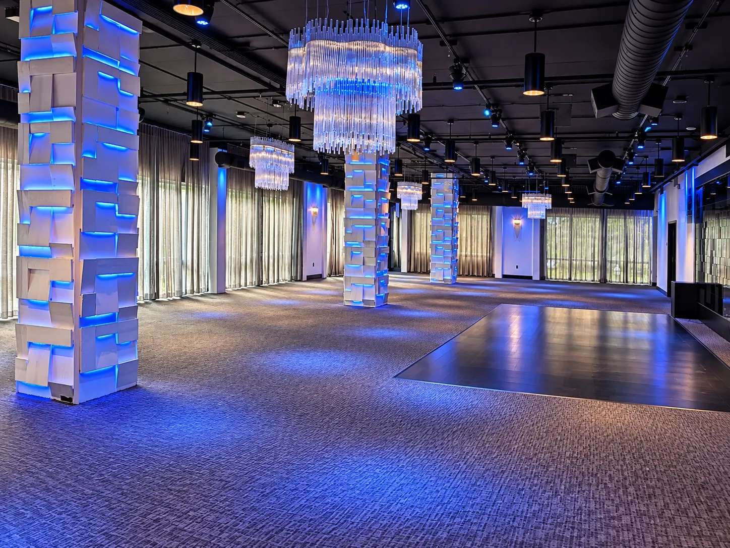 Wide view of the open Main Event Space at The MEZZ with a dark wood dance floor, crystal chandeliers and blue-lit architectural columns